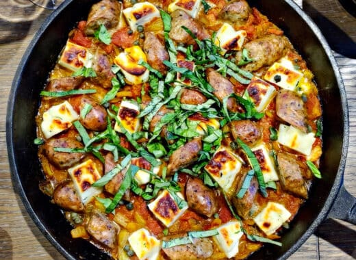 Cast iron skillet with baked Halloumi cheese, Italian sausage, and fresh basil in tomato sauce on table by The Hungry Songbird